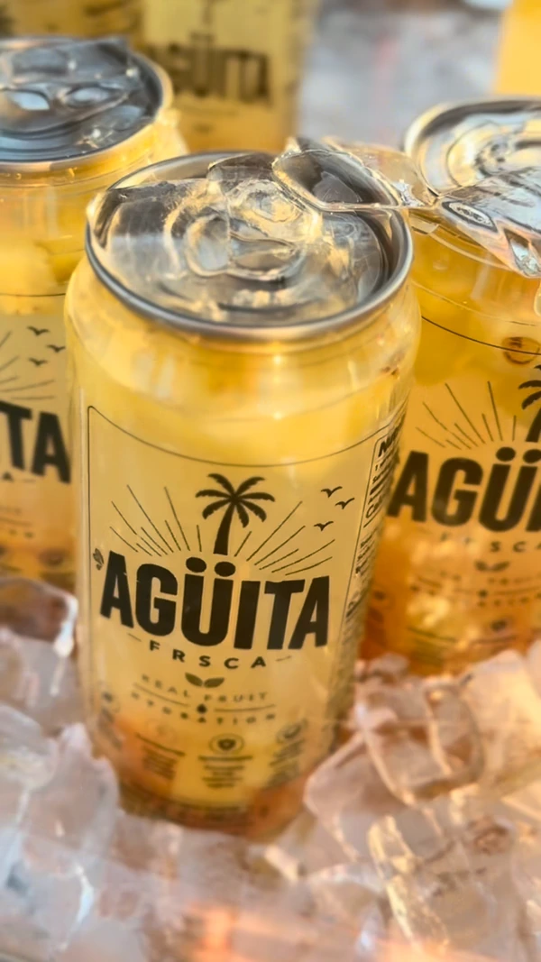 A close-up of yellow Agüita FRSCA cans chilled on ice