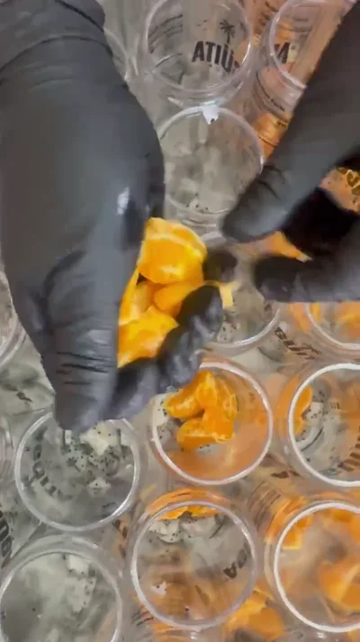 Gloved hands placing fresh orange pieces into an Agüita FRSCA can